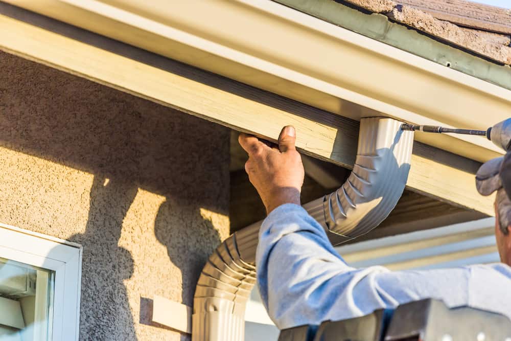 Professional technician performing gutter installation and securing a new downspout on a house roof