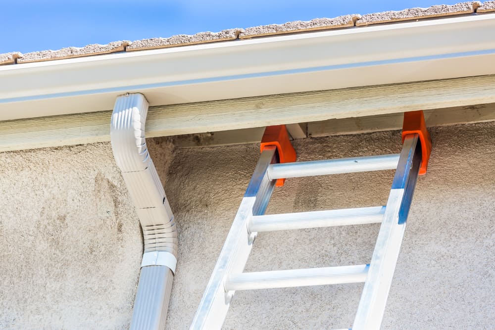 Aluminum gutter being secured to the eaves of a house with an extension ladder in place, highlighting professional gutter installation