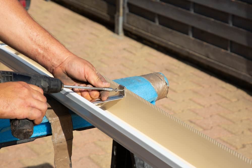 Close-up of a professional using a drill for gutter installation, demonstrating precise workmanship on a gutter section