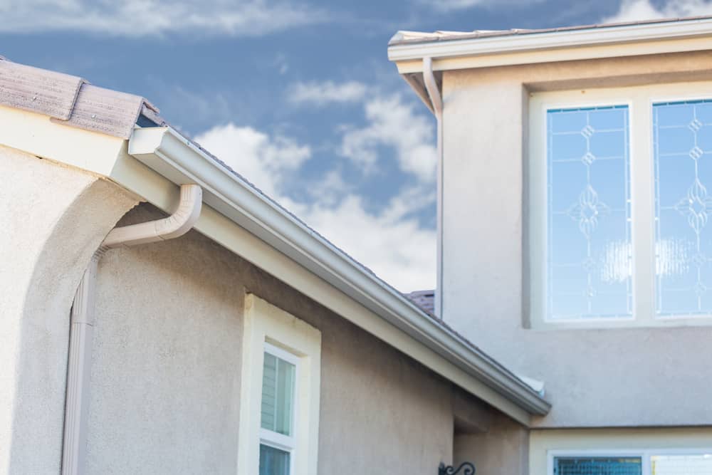 Gutter system at the edge of a residential roof with a clear blue sky in the background, showcasing gutter installation services