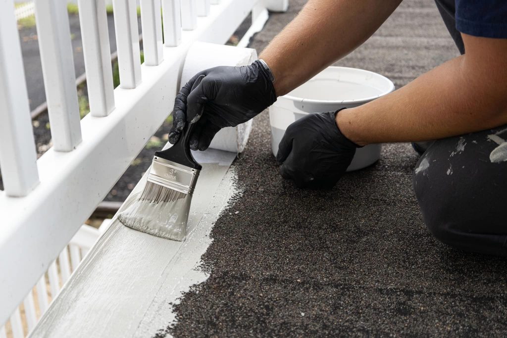 A professional contractor applies a high-quality fiberglass deck coating with non-slip decking paint to a residential patio surface, demonstrating the deck over paint process. The durable coating ensures extended life and beauty for the deck, showcasing Surf & Turf Roofing's expert fiberglass resurfacing service.