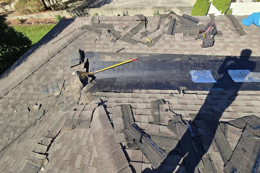 Roof leak repair near me in progress, with shingles removed to expose damaged roofing underlayment and prepare the area for repair. Tools are set up for replacing compromised shingles and sealing leaks effectively.